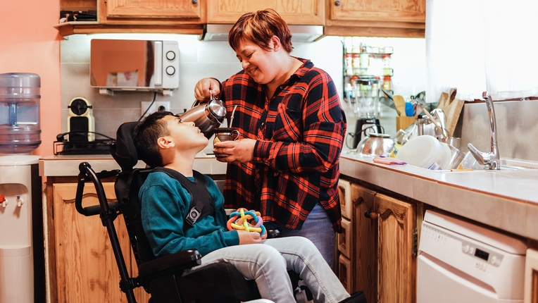 A support staff pouring a coffee for a boy with a disability