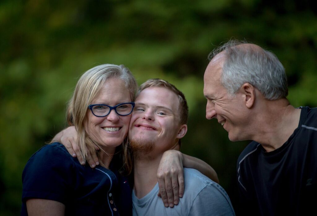 Boy with Down syndrome hugging his mom while his father stands beside him.